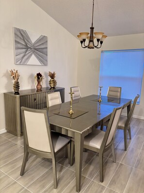 Une salle à manger avec une table rectangulaire, six chaises, un lustre et un élément décoratif mural.