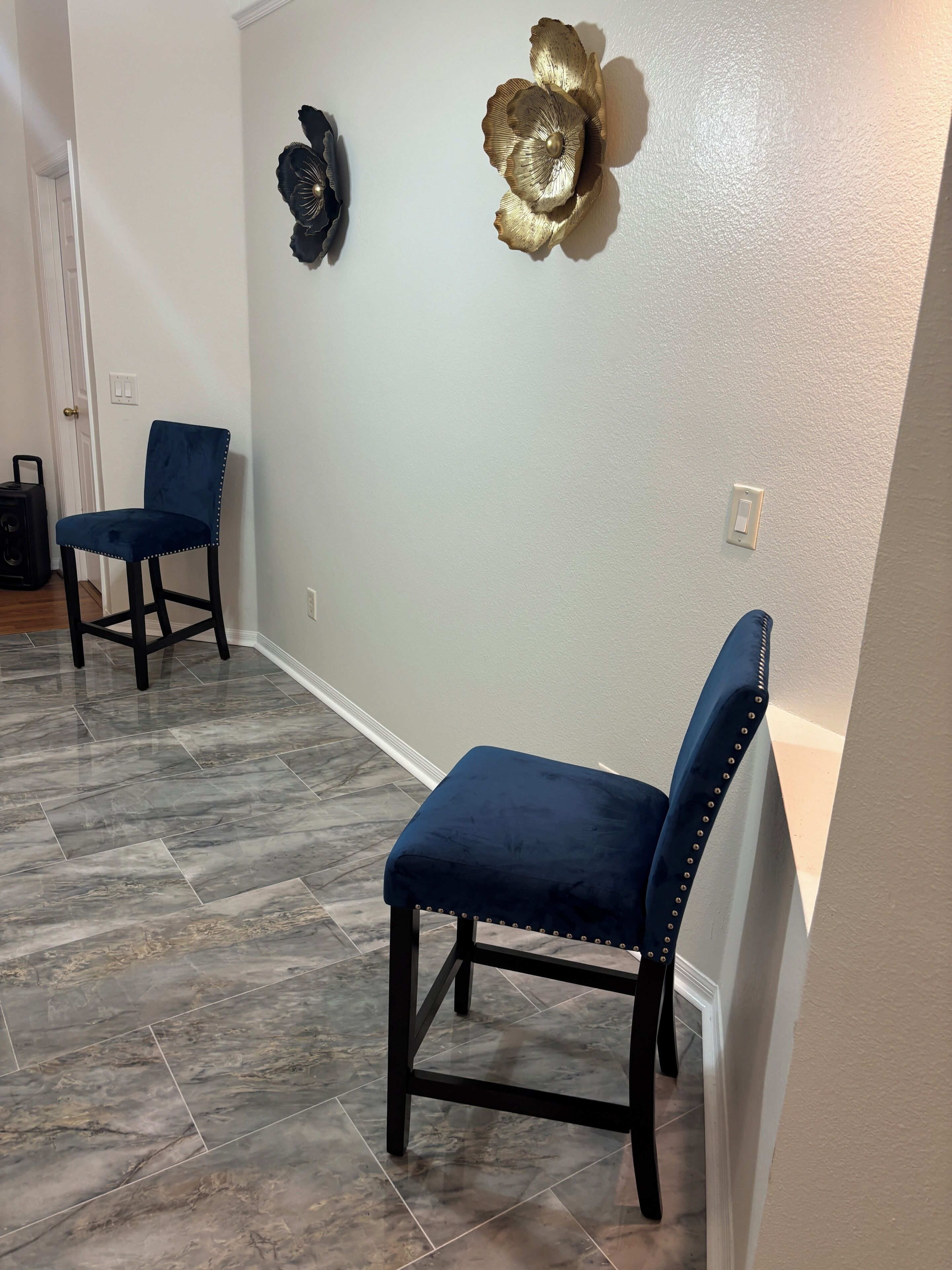A room with two blue upholstered chairs, a dark floor, and decorative wall art.