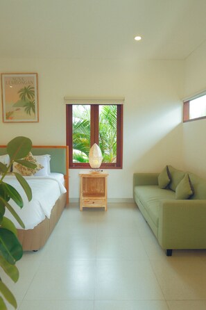 Un dormitorio con cama, sofá verde, mesita de noche, ventana con vistas a palmeras y un cuadro en la pared.