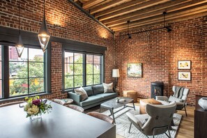 A spacious living area with a brick wall, large windows, a fireplace, and modern furniture. - Signature Loft Collection | Up to 20 Guests (Asheville)