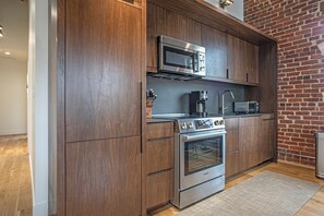 Een moderne keuken met houten kastjes, roestvrijstalen apparatuur en een bakstenen muur.