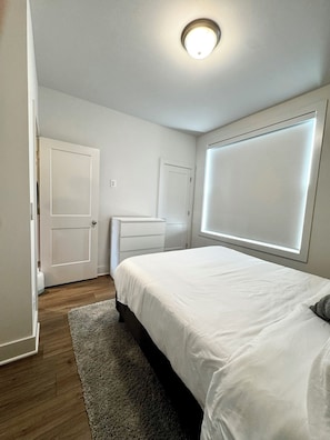 Un dormitorio con cama, cómoda, puerta y ventana con persianas.