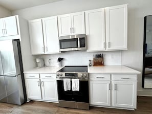 Una cocina moderna con armarios blancos, un refrigerador de acero inoxidable, un microondas, una estufa y un horno.