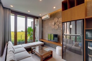 Una sala moderna con sofá, mesa de centro de vidrio, televisor de pantalla plana y refrigerador.