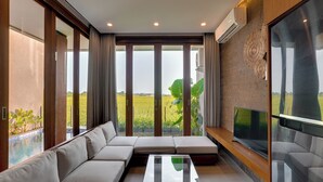 Una sala de estar moderna con un sofá seccional, un televisor de pantalla plana y un ventanal con vistas a un campo verde.