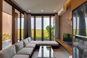 A modern living room with a sectional sofa, a flat-screen TV, and a large window offering a view of a green field.