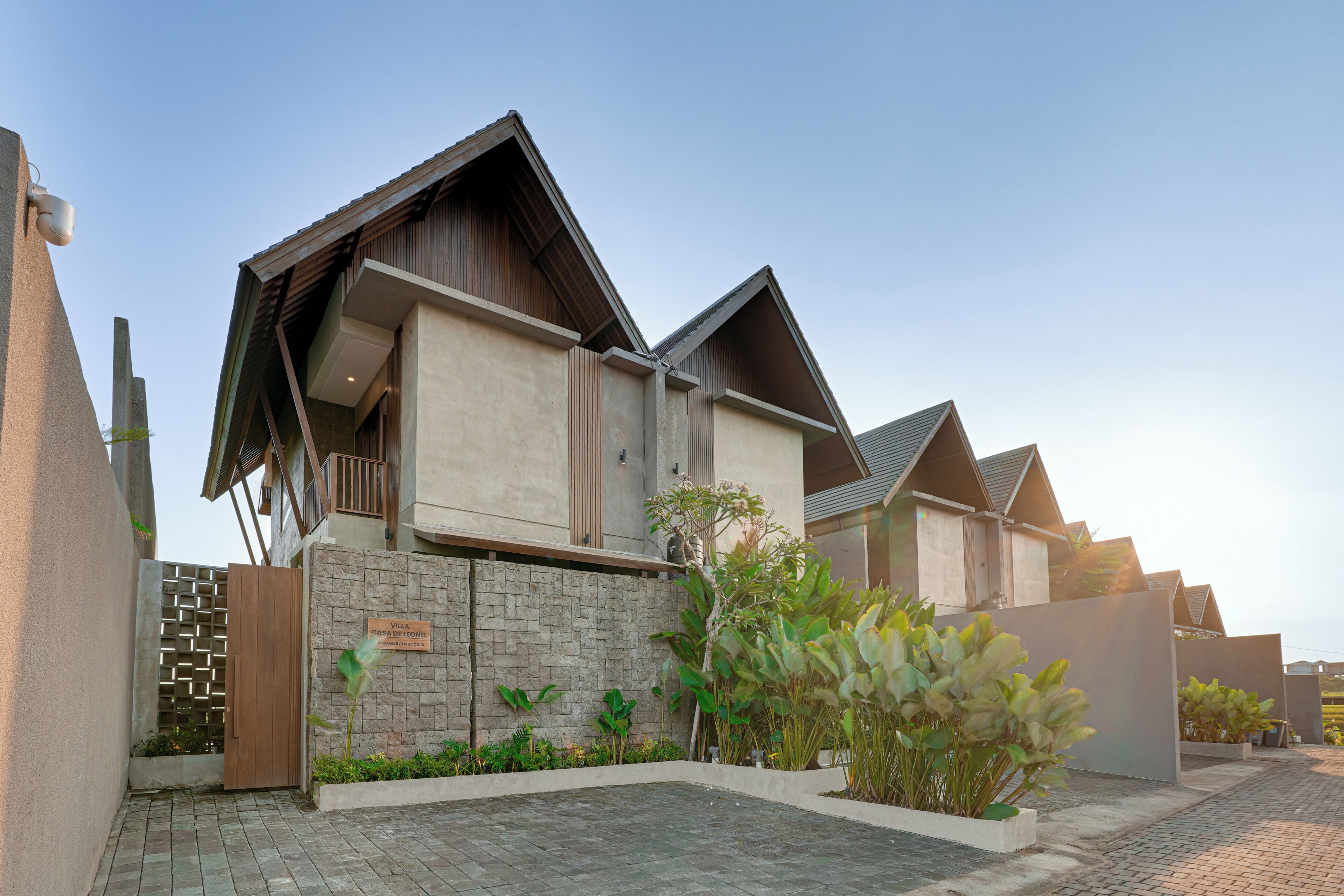 A modern villa with a stone facade, a wooden balcony, and a paved driveway.