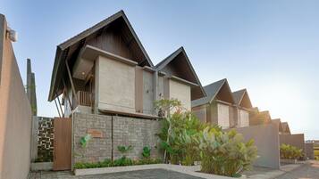 A modern villa with a stone facade, a wooden balcony, and a paved driveway.