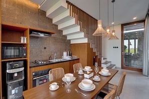 A modern kitchen with a dining area, featuring a wooden table set for a meal, a built-in oven, and a large window with a view.