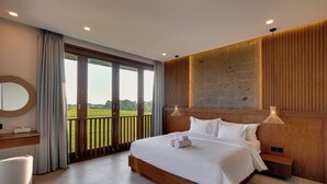 Habitación de hotel con una cama grande, cabecero de madera, vista a un campo verde a través de una puerta corredera, un espejo redondo y una mesita de noche.