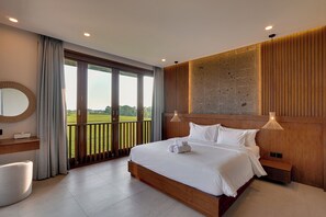A hotel room with a large bed, a wooden headboard, a view of a green field through a sliding door, a round mirror, and a bedside table.