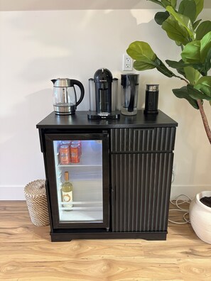Ein schwarzer Kühlschrank mit Glastür, darin eine Flasche und zwei Dosen.