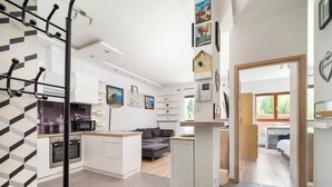 A modern kitchen with built-in appliances, a dining area with a grey sofa, and a hallway leading to a bedroom. - Royal Wilanów Charming Apartment (Warszawa)