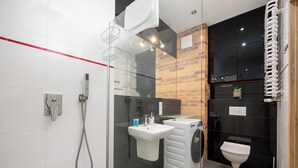 A modern bathroom with a glass shower enclosure, a white sink, a toilet, and a compact washing machine. - Royal Wilanów Charming Apartment (Warszawa)