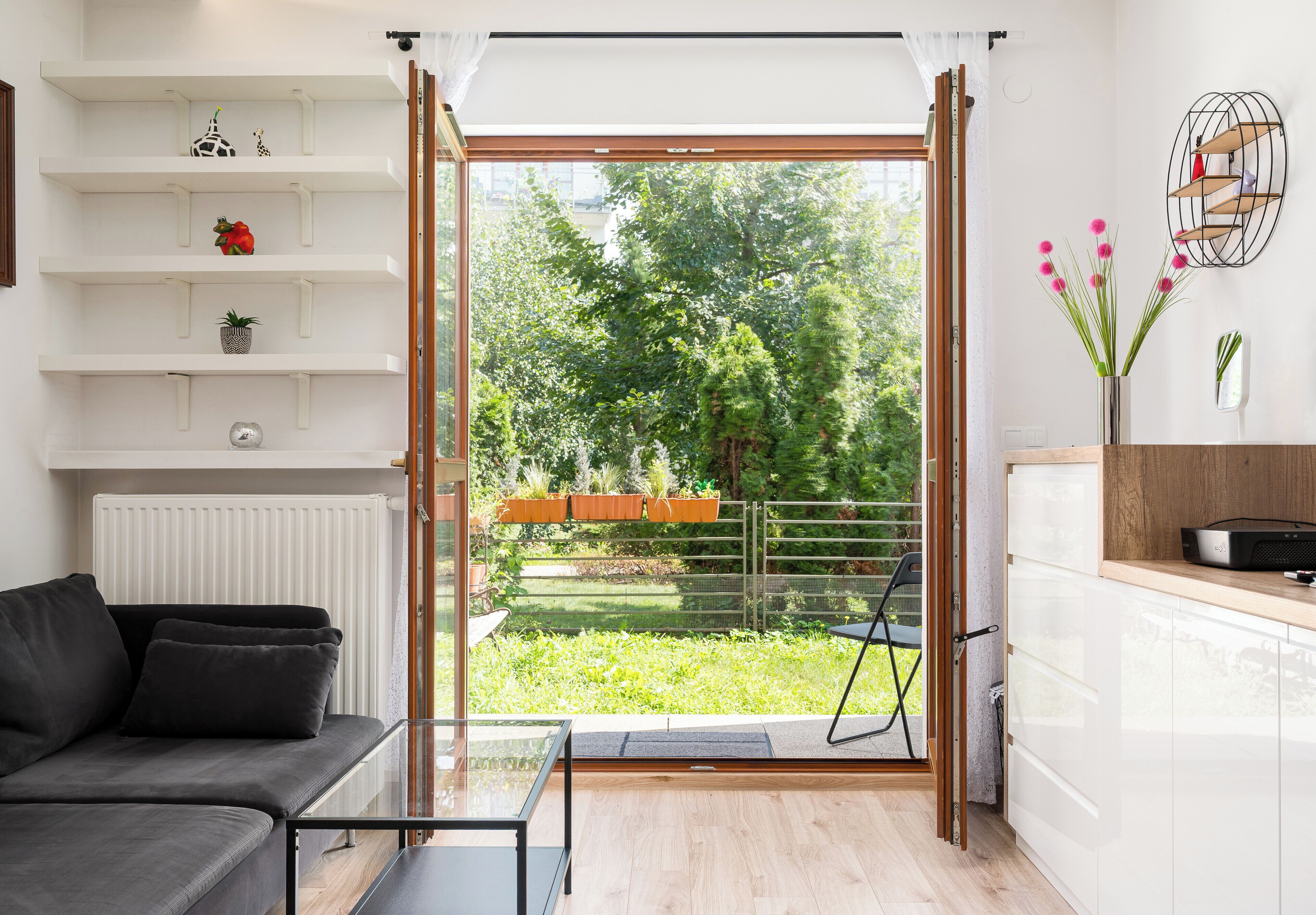 A modern living room with a sofa, a glass coffee table, and a view of a garden through a sliding door.