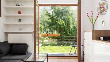 En moderne stue med sofa, sofabord i glas og udsigt til en have gennem en skydedør.
