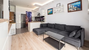 A modern living room with a grey sectional sofa, a glass coffee table, and a kitchen area in the background. - Royal Wilanów Charming Apartment (Warszawa)