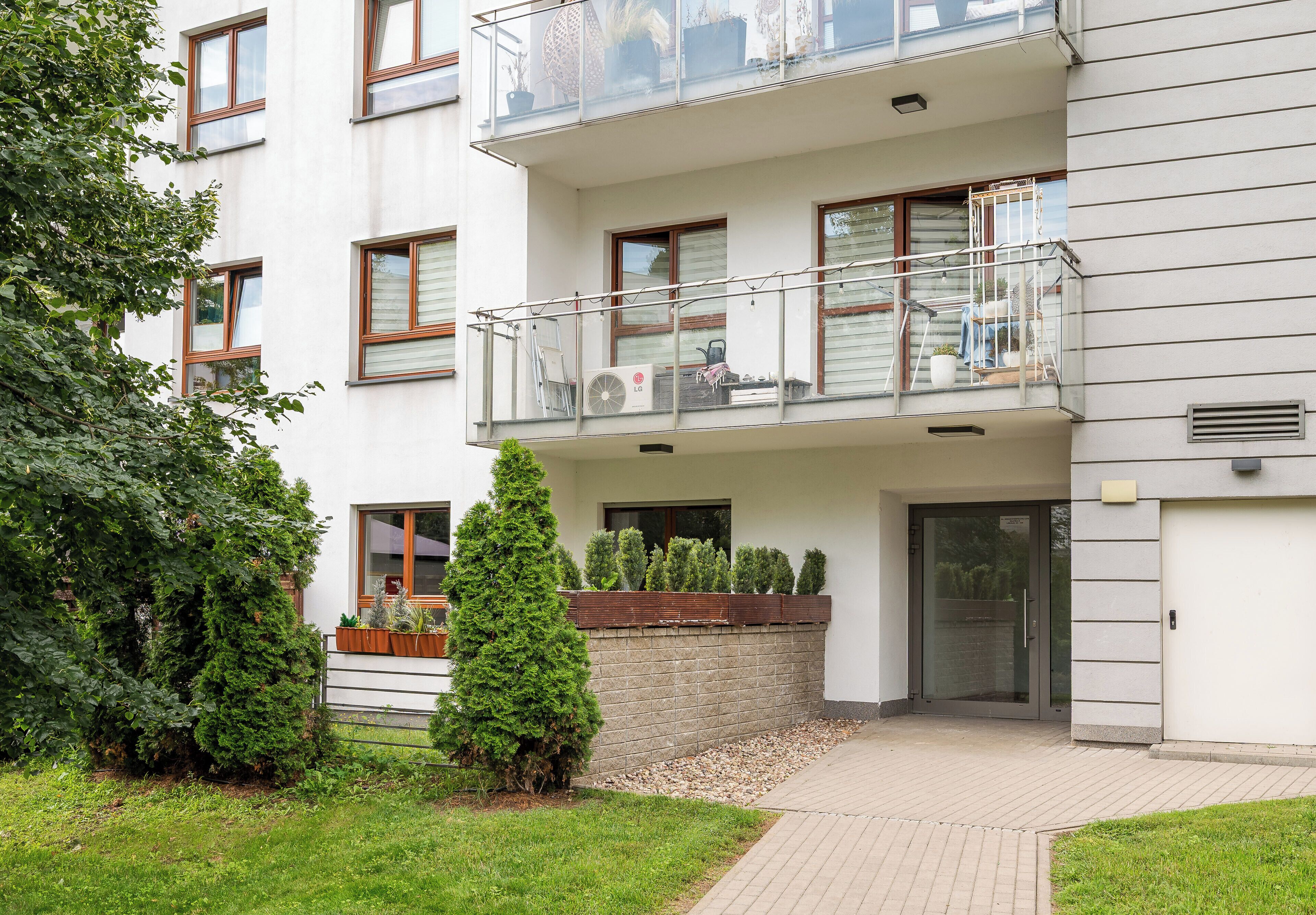 A multi-story residential building with a balcony, a brick wall, and a small garden area.