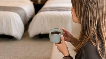 Une personne est assise sur un canapé dans une chambre d’hôtel qui comprend deux lits et une table de chevet avec une lampe.