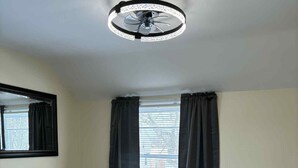 A bedroom with a bed, a dresser, a window with curtains, and a ceiling fan.