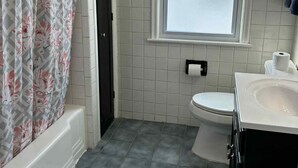 A bathroom with a shower curtain, a toilet, a sink, and a window with blinds.