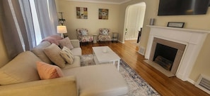 Een woonkamer met een bank, fauteuil en een open haard.
