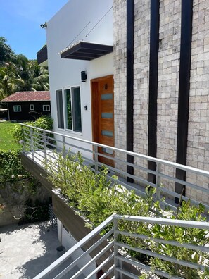 A modern building with a white facade, a wooden door with glass panels, and a stone wall. - Beautiful condo, on Roatán's best beach, just 3 minutes from everything!!🏖 (Roatan)