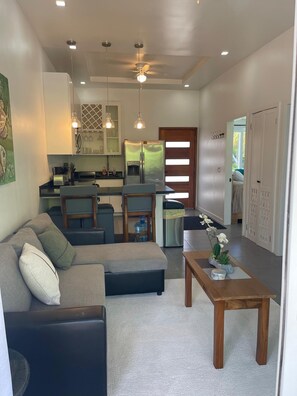 A modern living room with a sectional sofa, a wooden coffee table, and a dining area with a kitchen in the background. - Beautiful condo, located on Roatán's best beach, just 3 minutes from everything!!🏖 (Roatan)