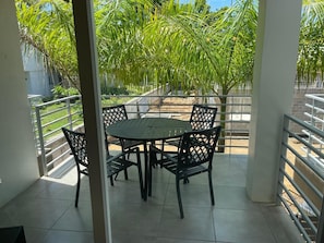 En overdækket terrasse med et rundt bord og fire stole, omgivet af gelænder.
