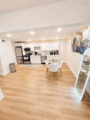 A modern kitchen with white cabinetry, stainless appliances, and a dining area with a glass table and white chairs. - The Ascended Retreat (Dallas)