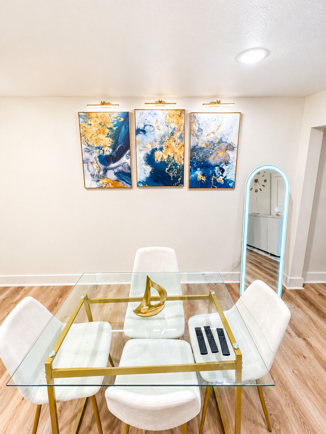 A modern dining area with a glass table, white chairs, and gold accents.