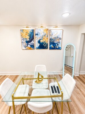 A modern dining area with a glass table, white chairs, and gold accents. - The Ascended Retreat (Dallas)