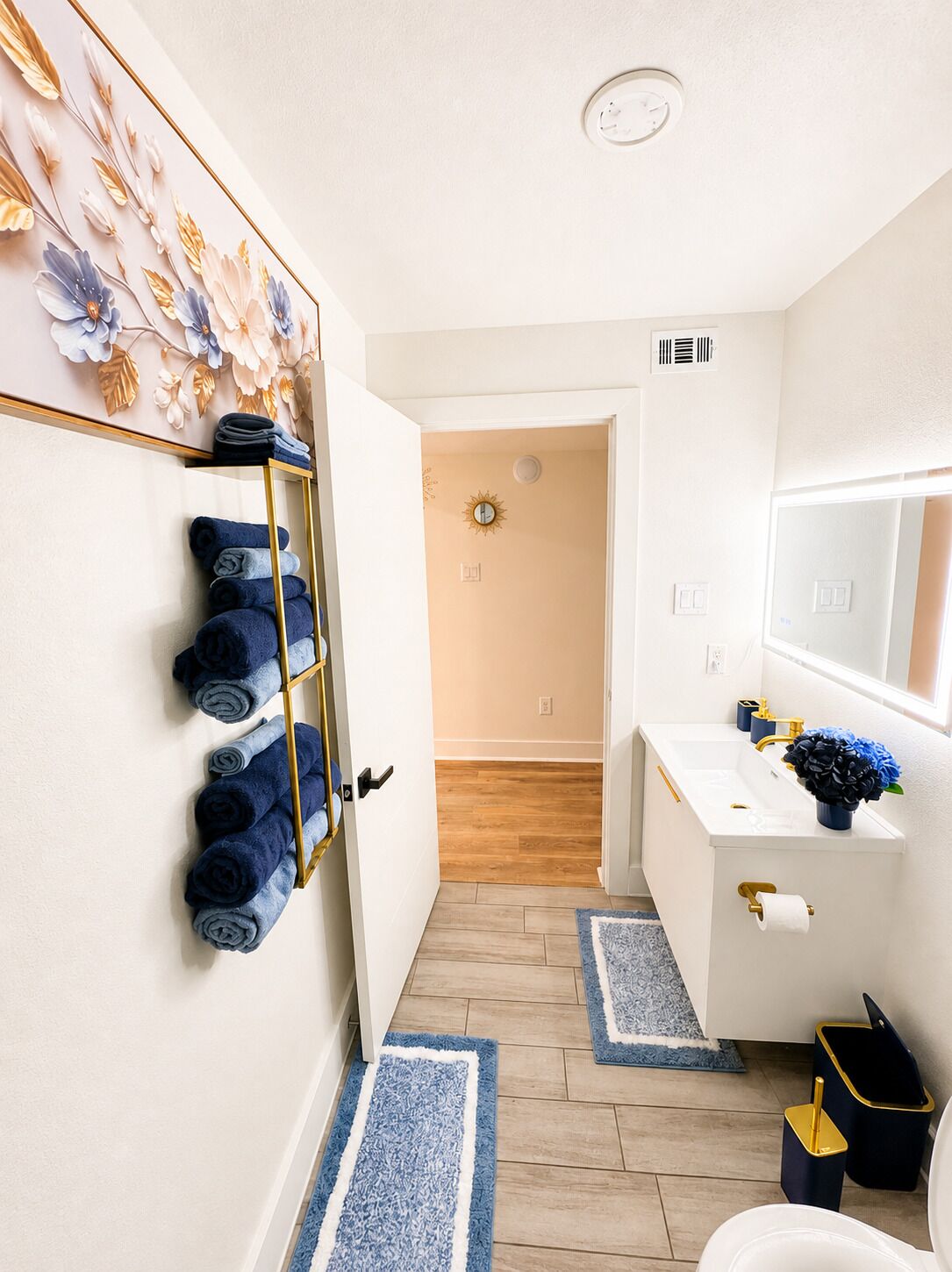 Une salle de bain avec un lavabo blanc, des serviettes bleues, un miroir et un tapis bleu et blanc.
