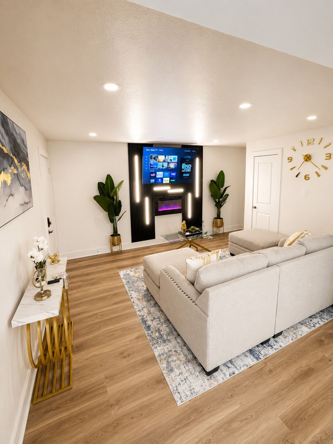 A modern living room with a sofa, a coffee table, a TV mounted on the wall, and a door with a clock.
