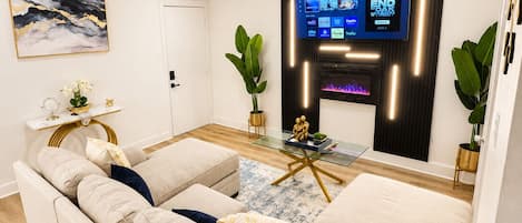 Una sala de estar moderna con un sofá seccional color beige, una mesa de centro de vidrio y un televisor de pantalla plana montado en la pared.