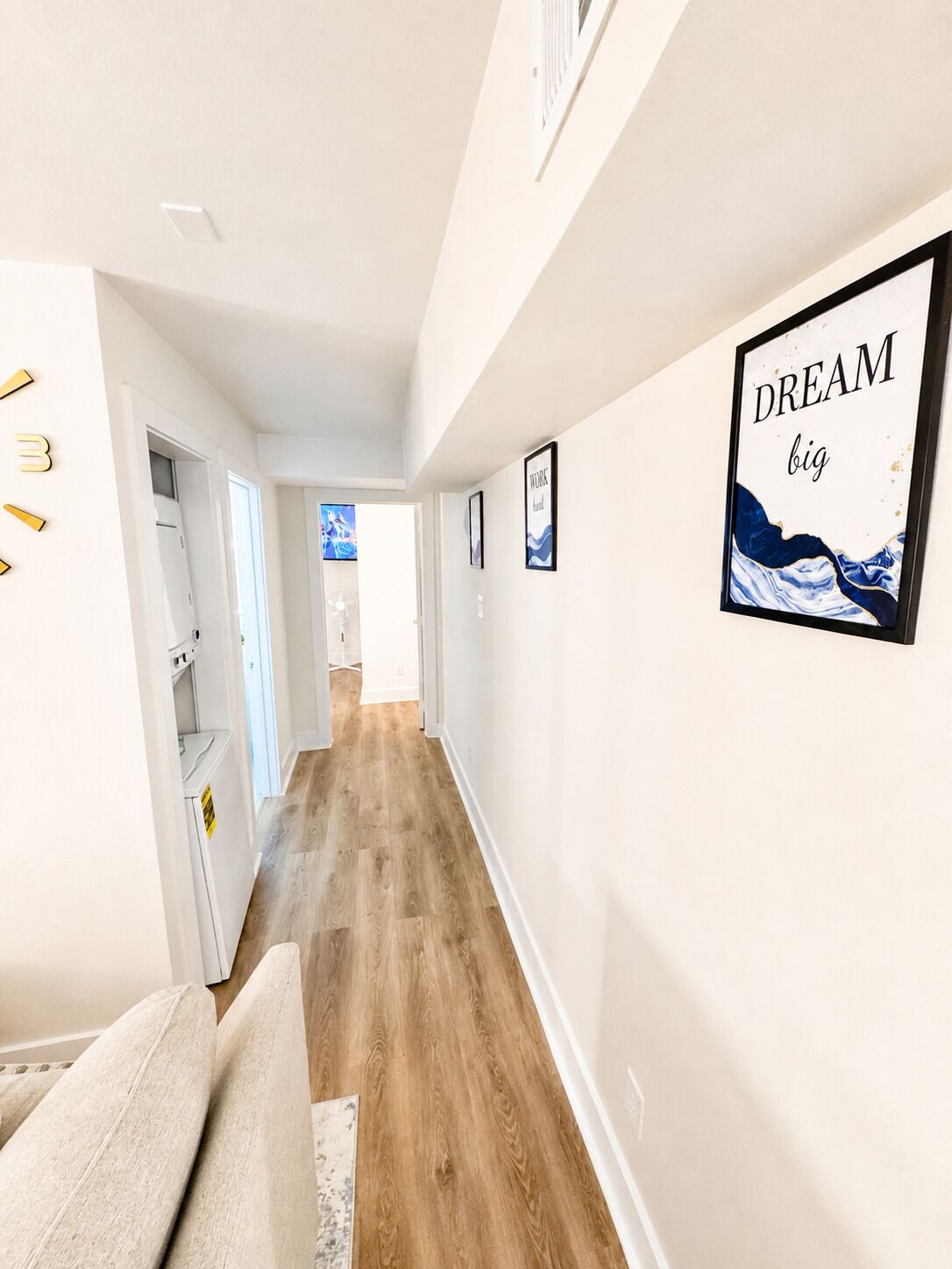 A hallway with a wooden floor, white walls, and framed artwork including a 'DREAM big' sign.