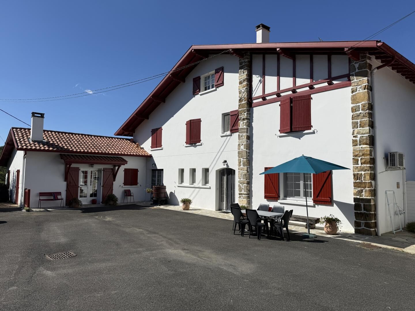 Un edificio de dos pisos con fachada de piedra, contraventanas rojas y techo de tejas.