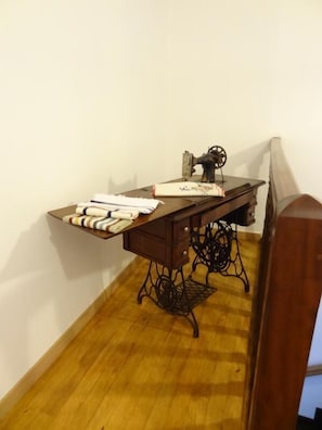 Ein Eckzimmer mit Holzboden, einer Nähmaschine und einem kleinen Tisch mit gefalteter Kleidung.