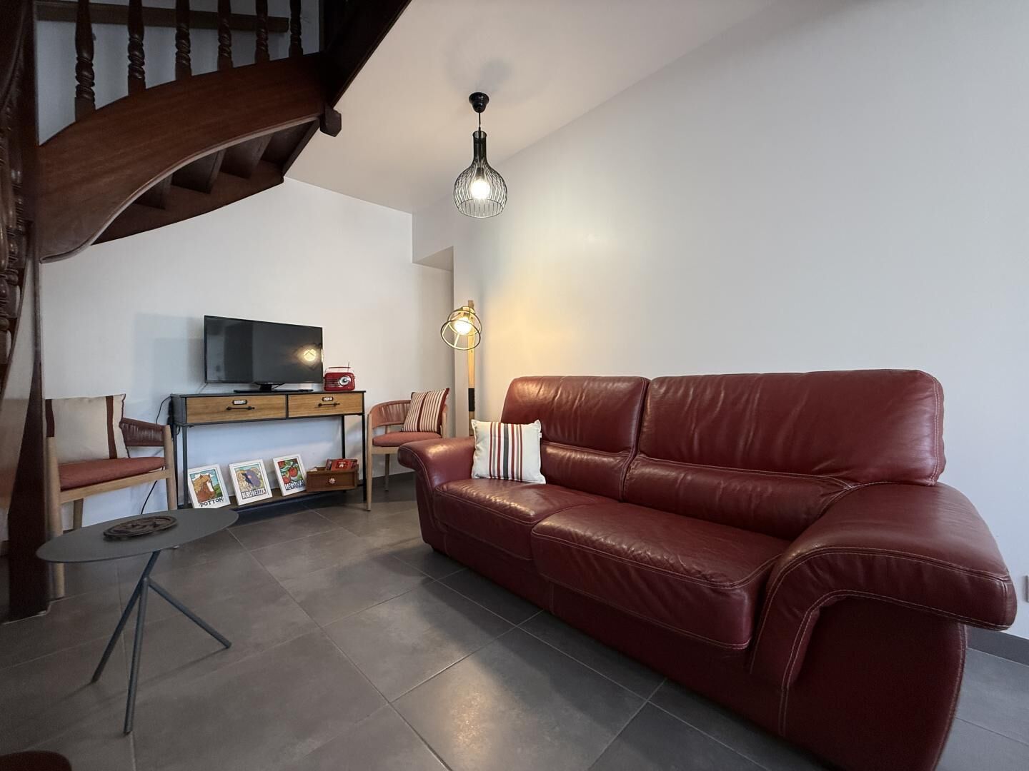 A modern living room with a leather sofa, a wooden coffee table, a TV on a wooden stand, and a staircase.