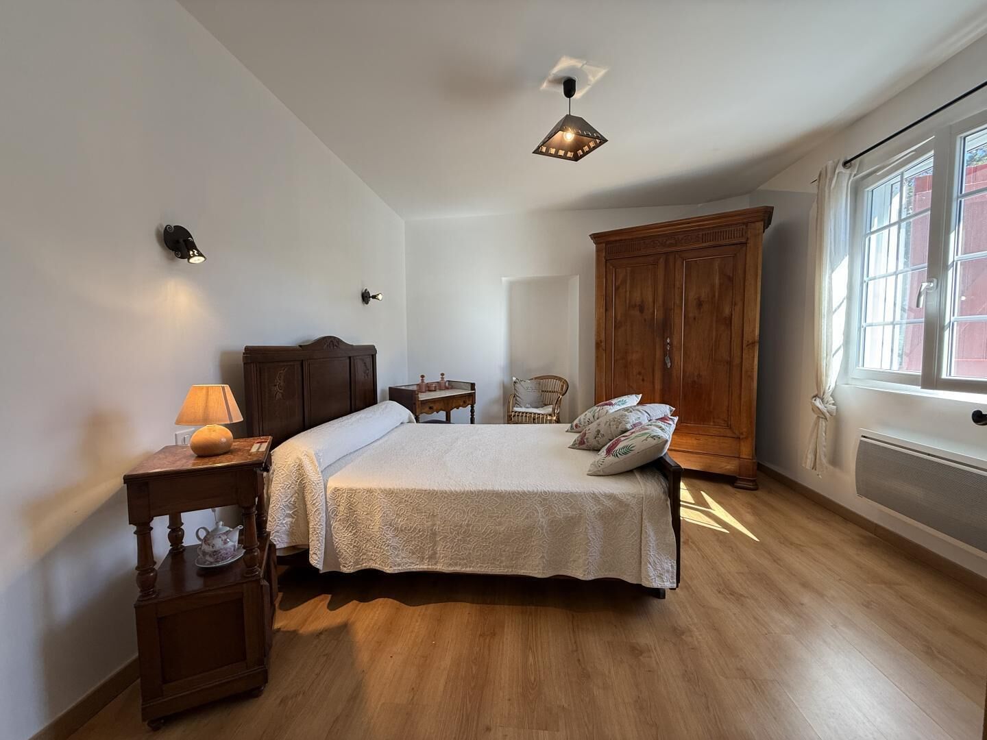 A bedroom with a bed, bedside table, lamp, wardrobe, and a window with curtains.