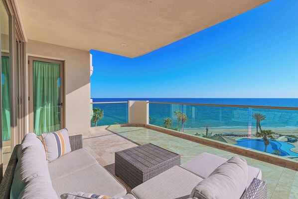 Ein Balkon mit Blick auf den Ozean, ein Pool und eine Sitzecke mit Kissen.