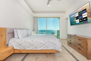 Ein Schlafzimmer mit einem Bett, einem an der Wand befestigten Fernseher und Meerblick durch große Fenster.