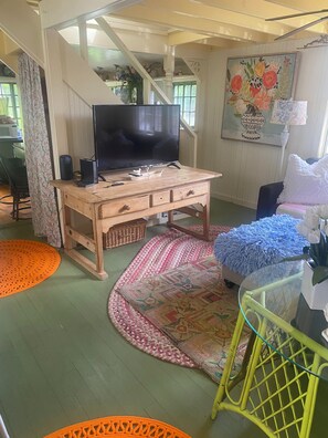 A cozy living room with a wooden TV stand, a flat-screen TV, a woven basket, and a variety of colorful rugs. - Princess of The Lake (Caroga Lake)