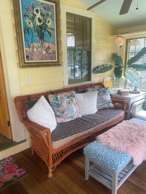 A wicker sofa with patterned cushions, a small table with decorative items, and a window with a view. - Princess of The Lake (Caroga Lake)