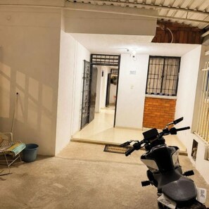 A scooter parked in a narrow hallway with a tiled floor, a metal gate, and a brick wall.
