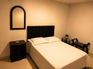 A bedroom with a bed, a nightstand, a mirror, a small table with a plant, and a bench. - Vrbo Property (Valledupar)