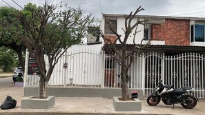 A gated residential area with a white fence, a motorcycle parked in front, and a tree in a planter. - Vrbo Property (Valledupar)