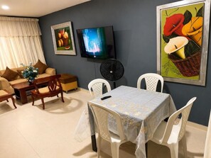 A living room with a sofa, a dining table with chairs, a TV, and a painting on the wall. - Vrbo Property (Valledupar)