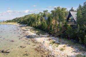 A lakeside property with a wooden deck and a stone pathway leading to a cabin. - Northport Noir | Waterfront Aframe Retreat (Northport)