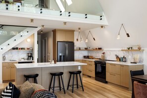 Eine moderne Küche mit Kochinsel, Barhocker, Backofen und Edelstahl-Kühlschrank.